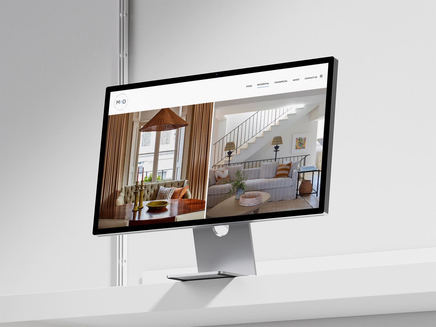 A computer monitor on a white shelf displays an interior design website featuring images of a dining area and a living room.