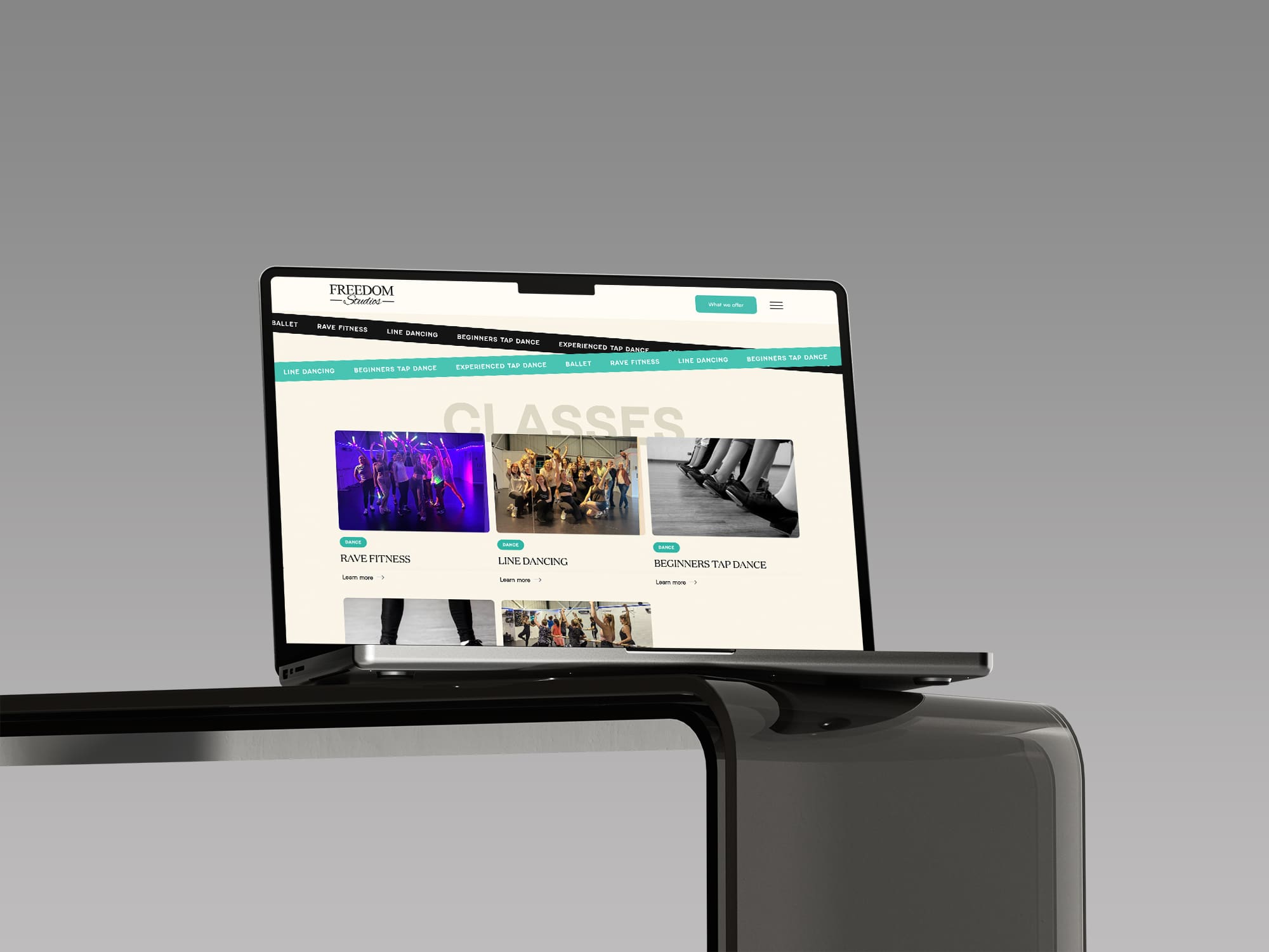 A laptop on a black table displays a dance studio website offering group fitness, line dancing, and beginner tap dance classes.