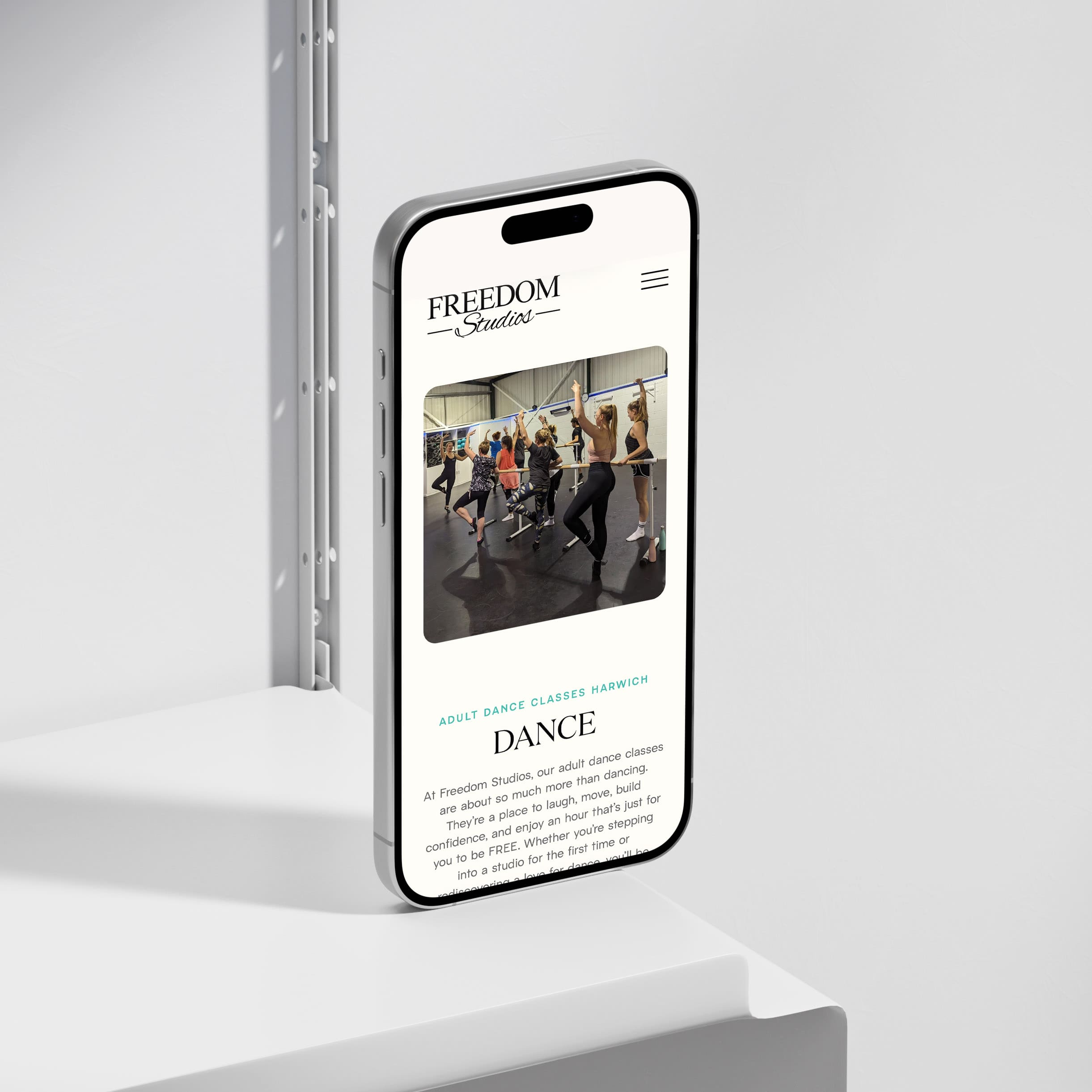 A smartphone displays the Freedom Studios website showing a group dance class with several people following an instructor in a studio.