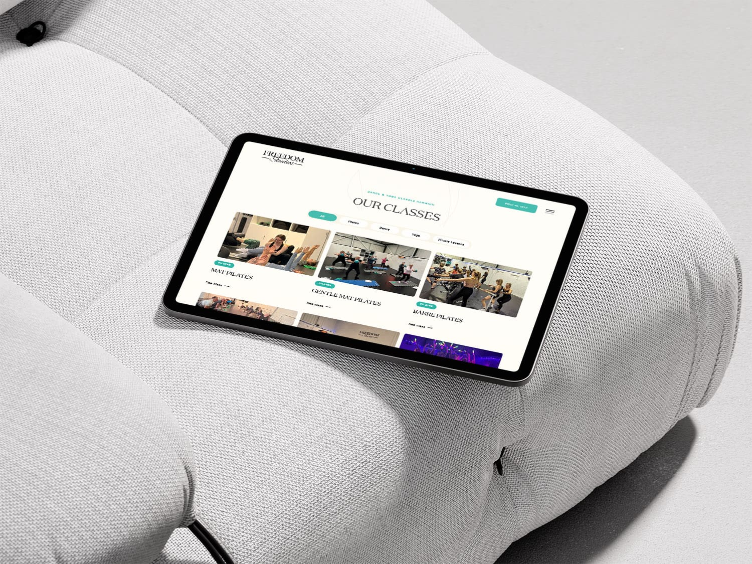A tablet displaying a website section titled “Our Classes” rests on a light gray upholstered couch.