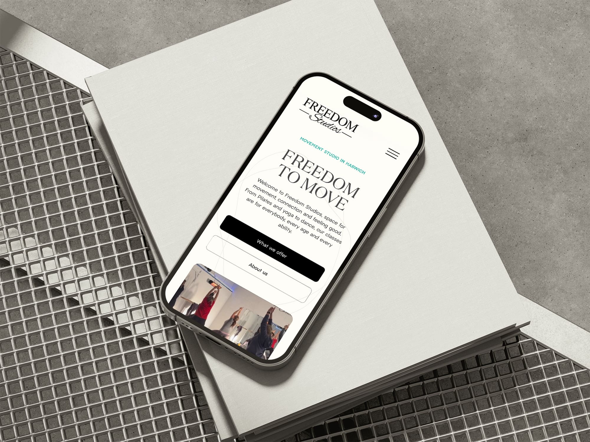 A smartphone displaying the “Freedom Central” website—crafted by a skilled freelance web designer—rests on stacked books placed on a metal grid surface.